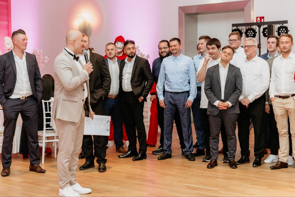 Hochzeitsmoderator mit Mikrofon f&uuml;hrt durch das Abendprogramm vor einer Gruppe G&auml;ste
